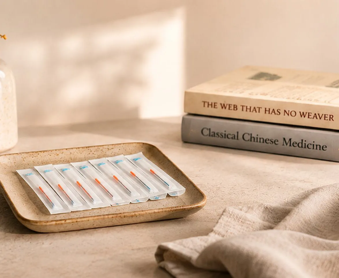 Sterile acupuncture needles on a ceramic tray beside books on Classical Chinese Medicine
