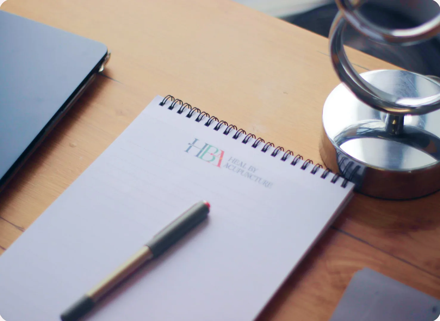 Heal By Acupuncture branded notebook and pen on a treatment room desk